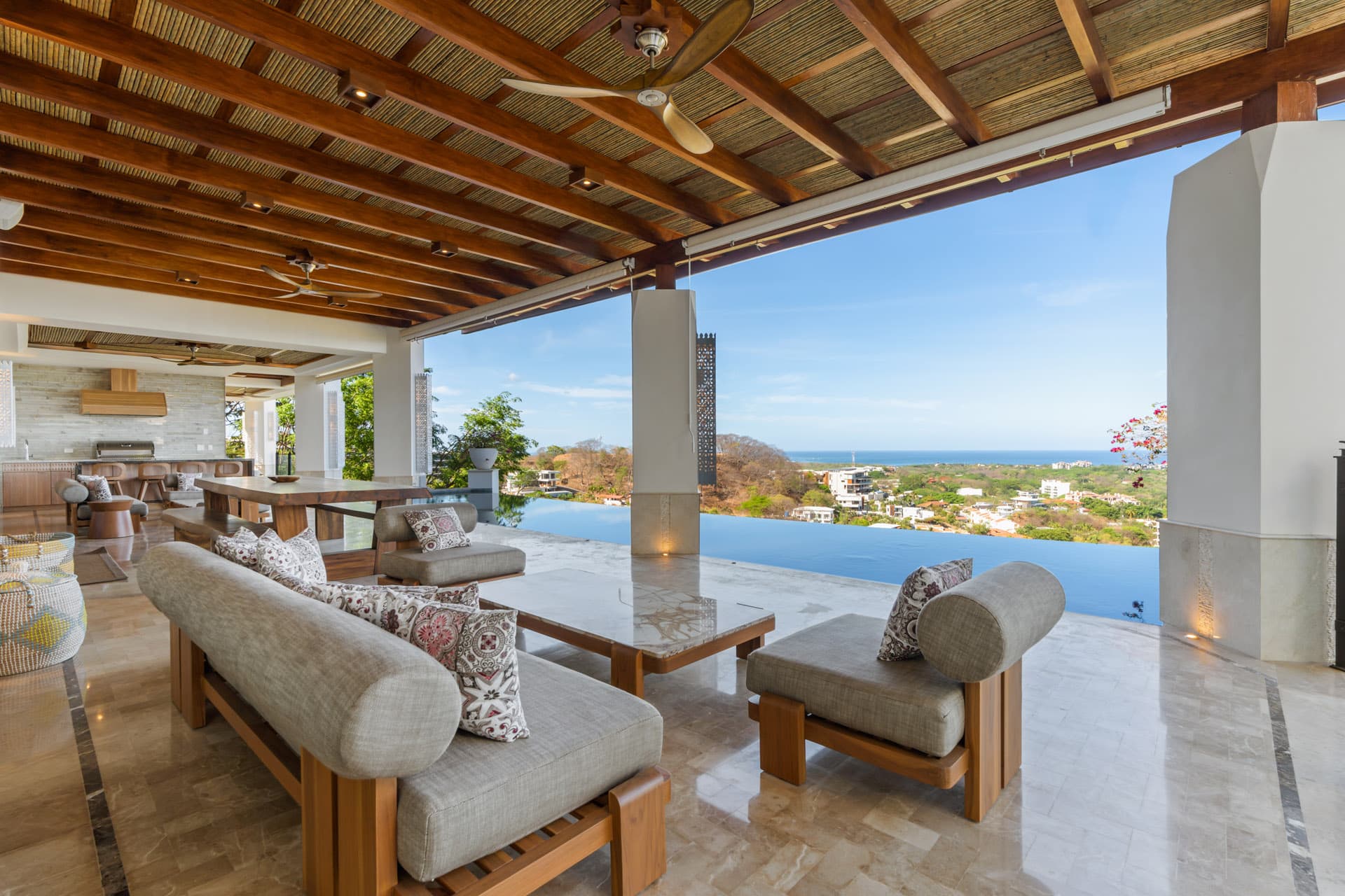 Covered pool terrace at Villa Luciérnaga — outdoor seating, open-air kitchen, and Tamarindo Bay stretching to the Pacific horizon