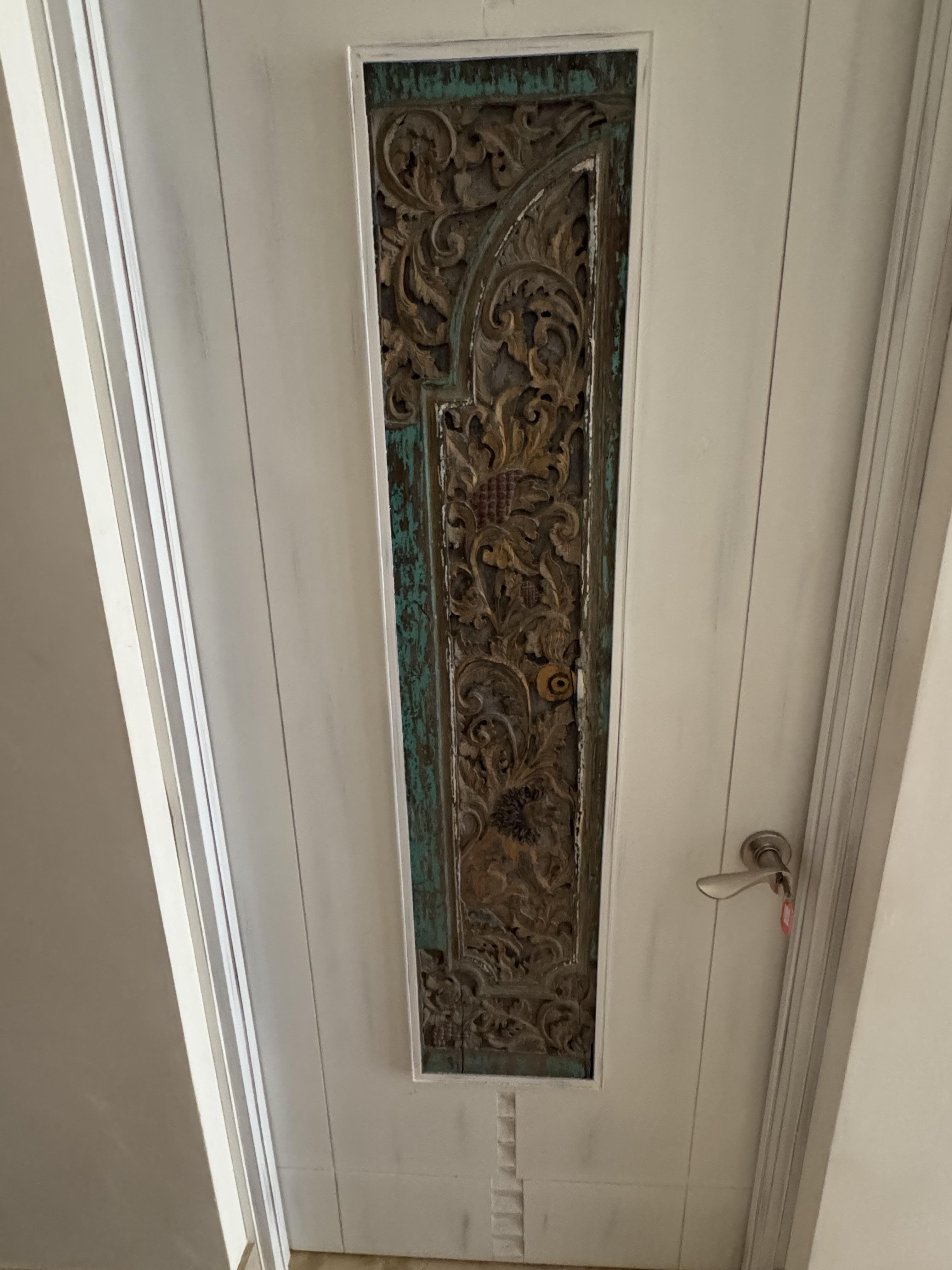 Antique Thai carved wood panel -- lion motif with dense teal botanical scrollwork, installed on a bedroom door