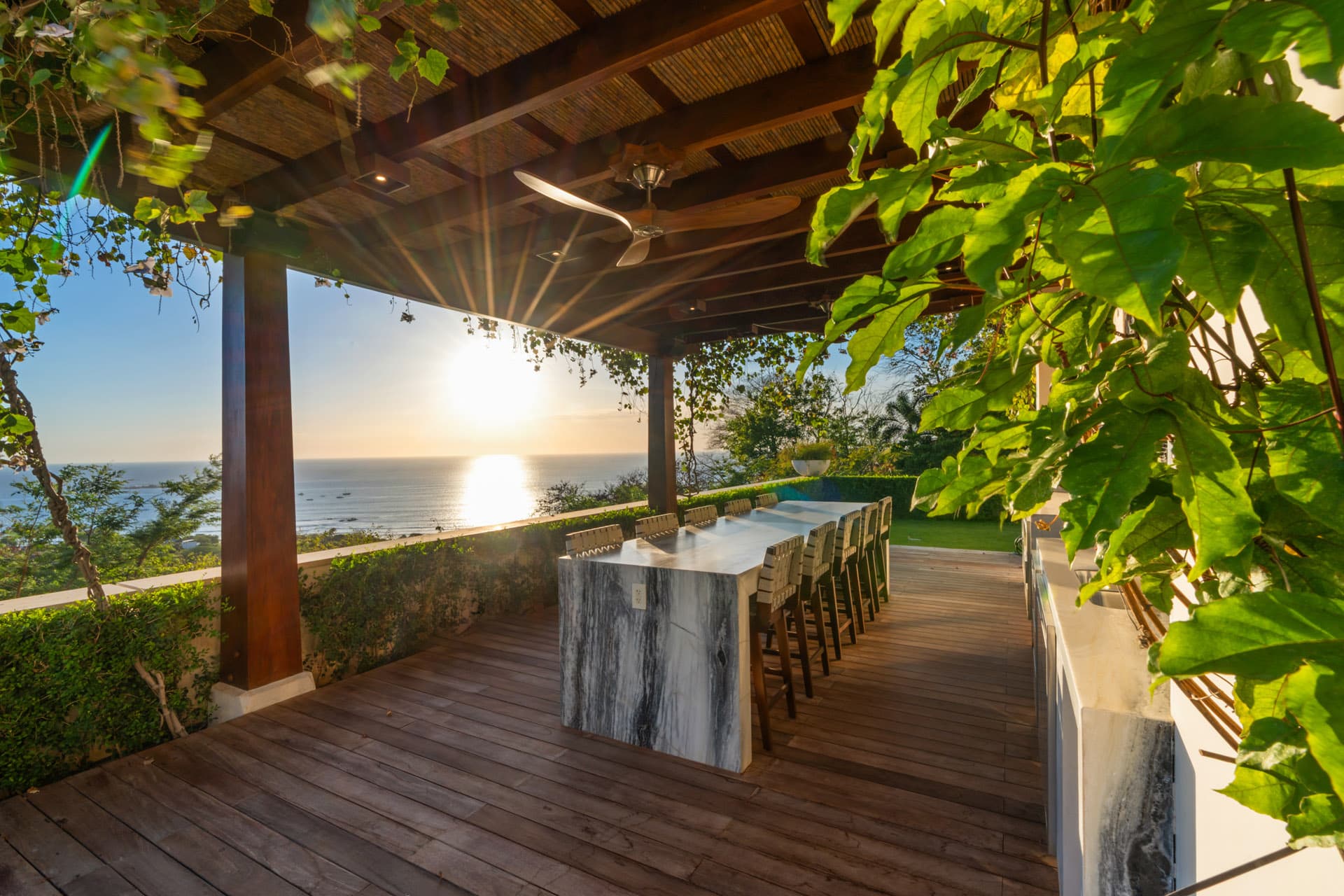 Lower deck bar at Villa Luciérnaga at sunset -- marble island bar, vine pergola overhead, Pacific sunset and Tamarindo Bay in the background