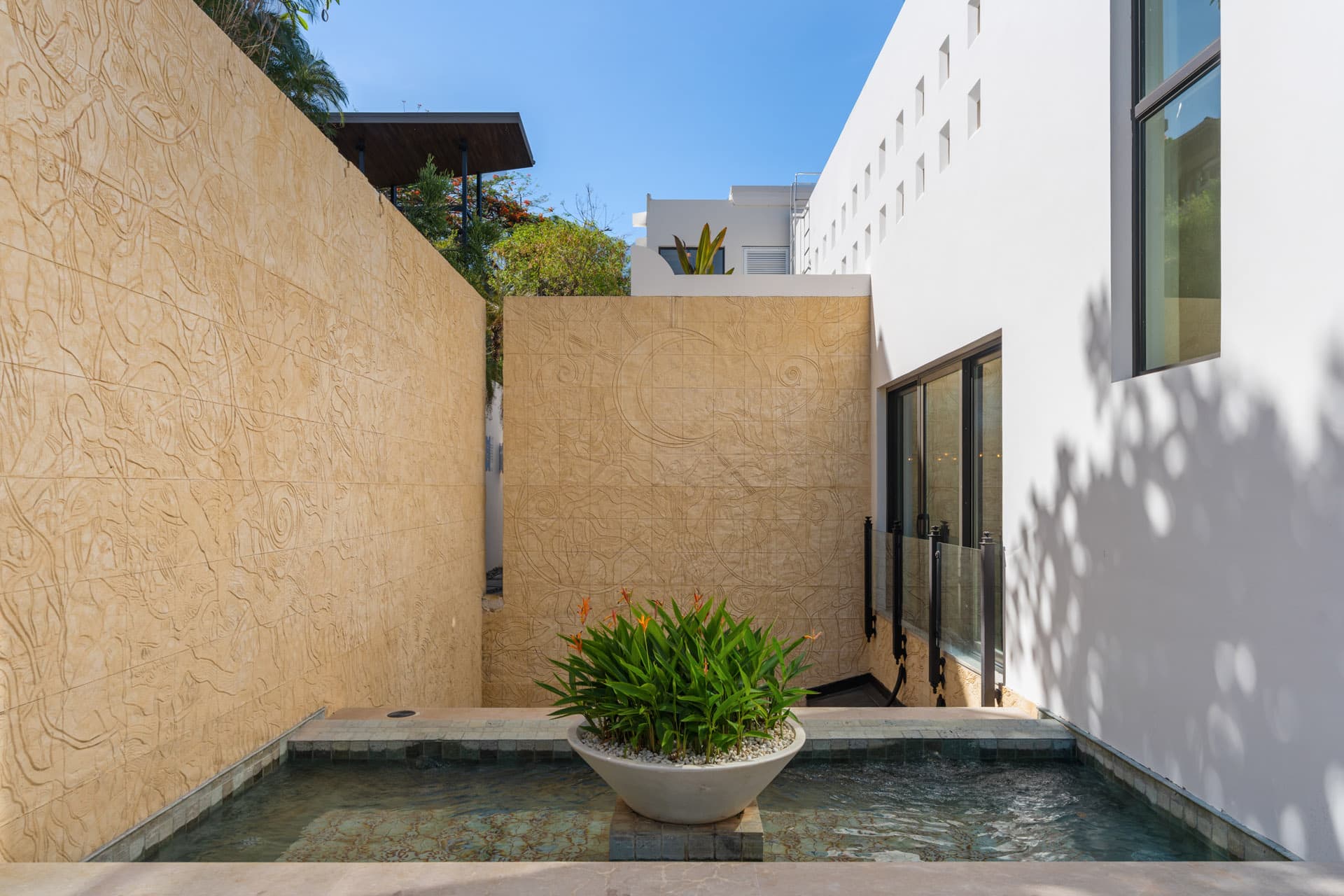 Private outdoor shower courtyard at Villa Luciérnaga -- bas relief carved stone walls, shallow reflecting pool, and tropical plantings