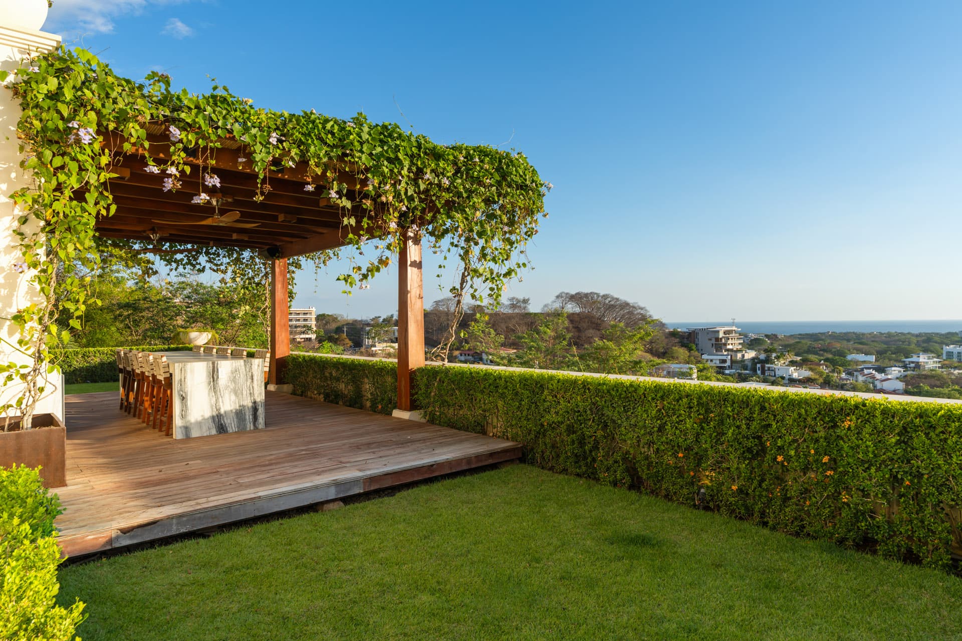 Lower deck pergola at Villa Luciérnaga at golden hour -- vine-covered teak structure, marble bar island, ocean horizon