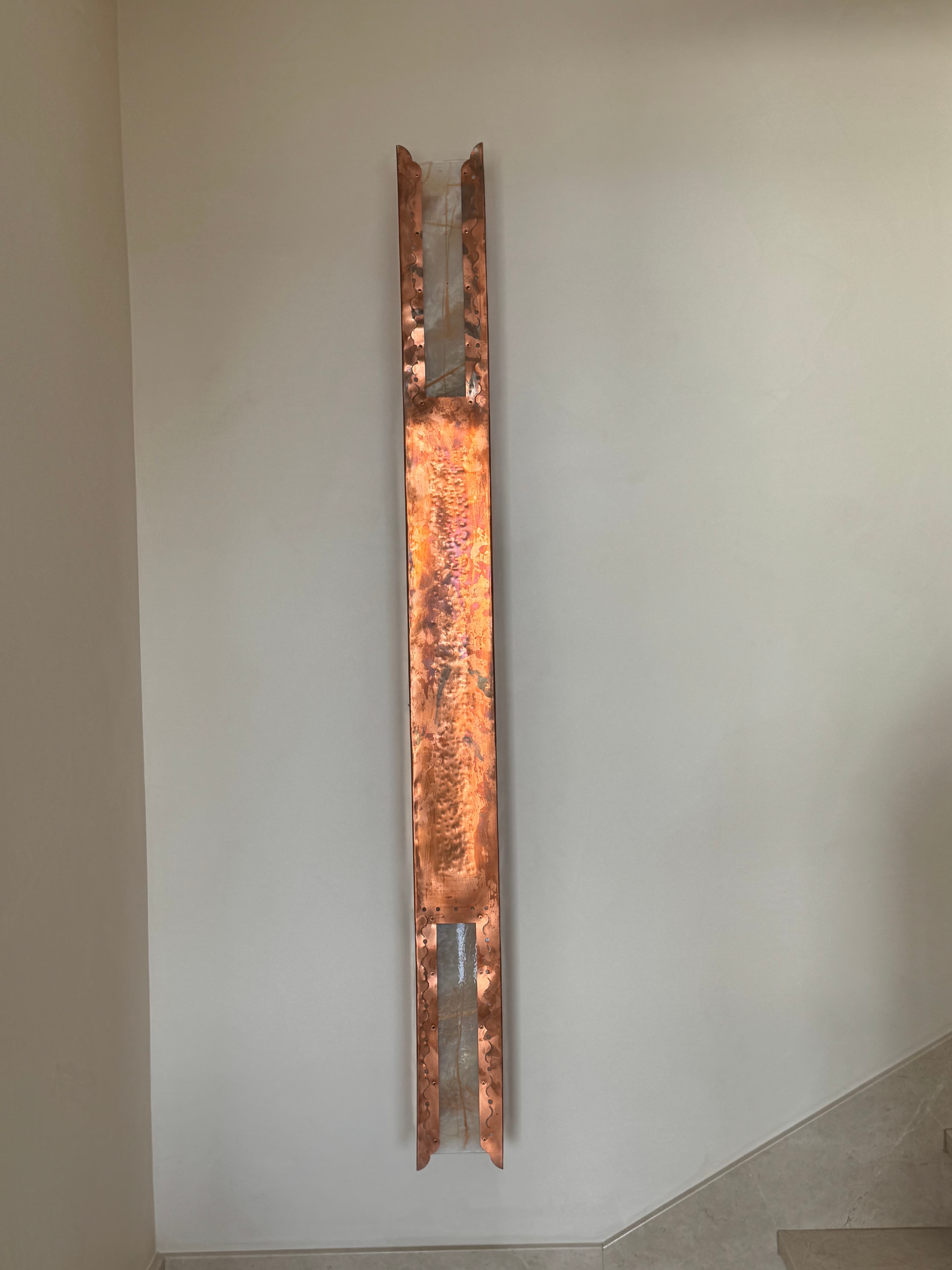 Hammered copper wall sconce at Villa Luciérnaga -- long horizontal form with onyx glass inserts at each end, hand-fabricated by the architect's family