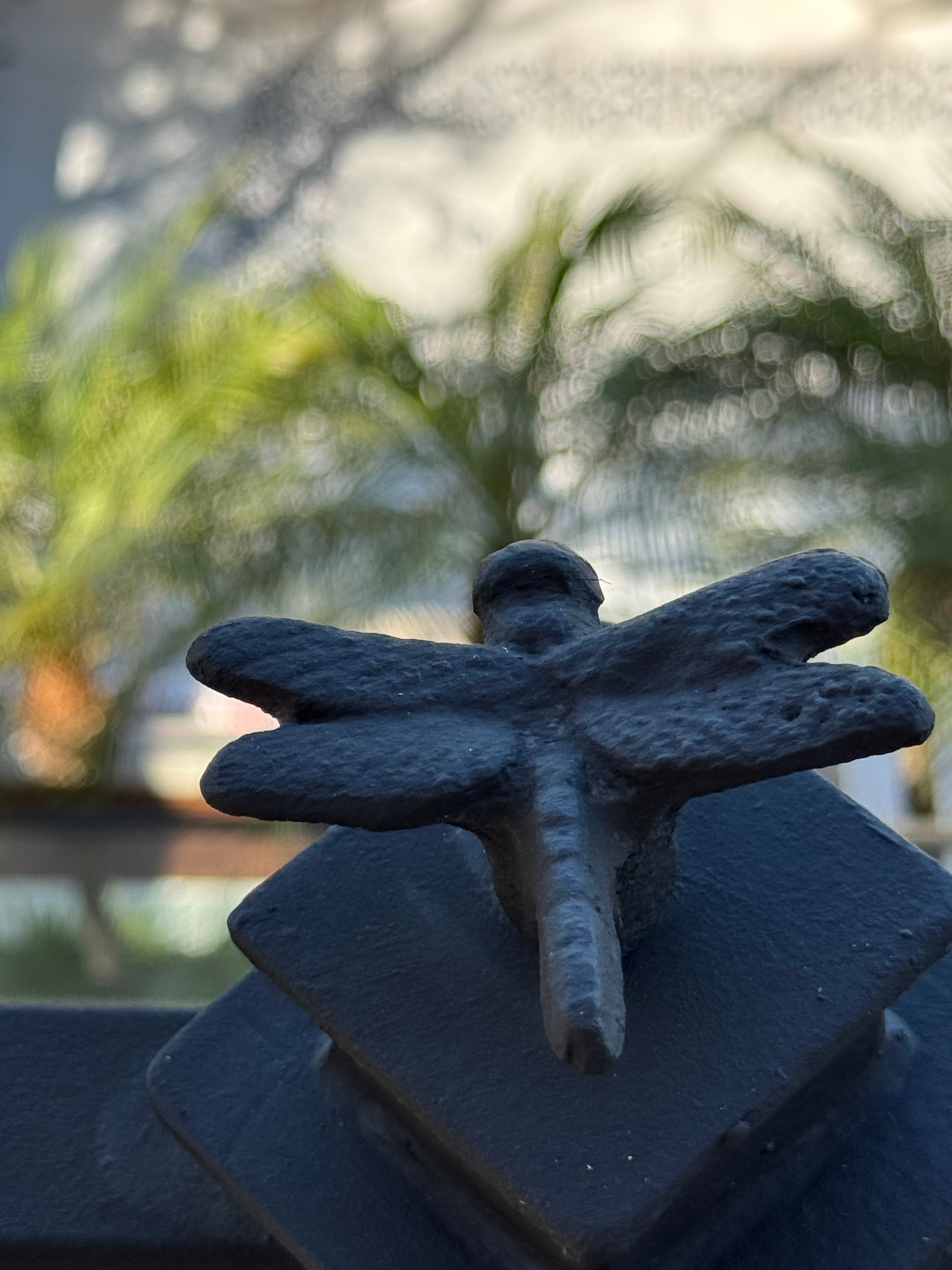 Iron firefly ornament atop a glass railing post at Villa Luciérnaga -- small sculptures fixed to every post across the entire property, wings and body rendered in detail
