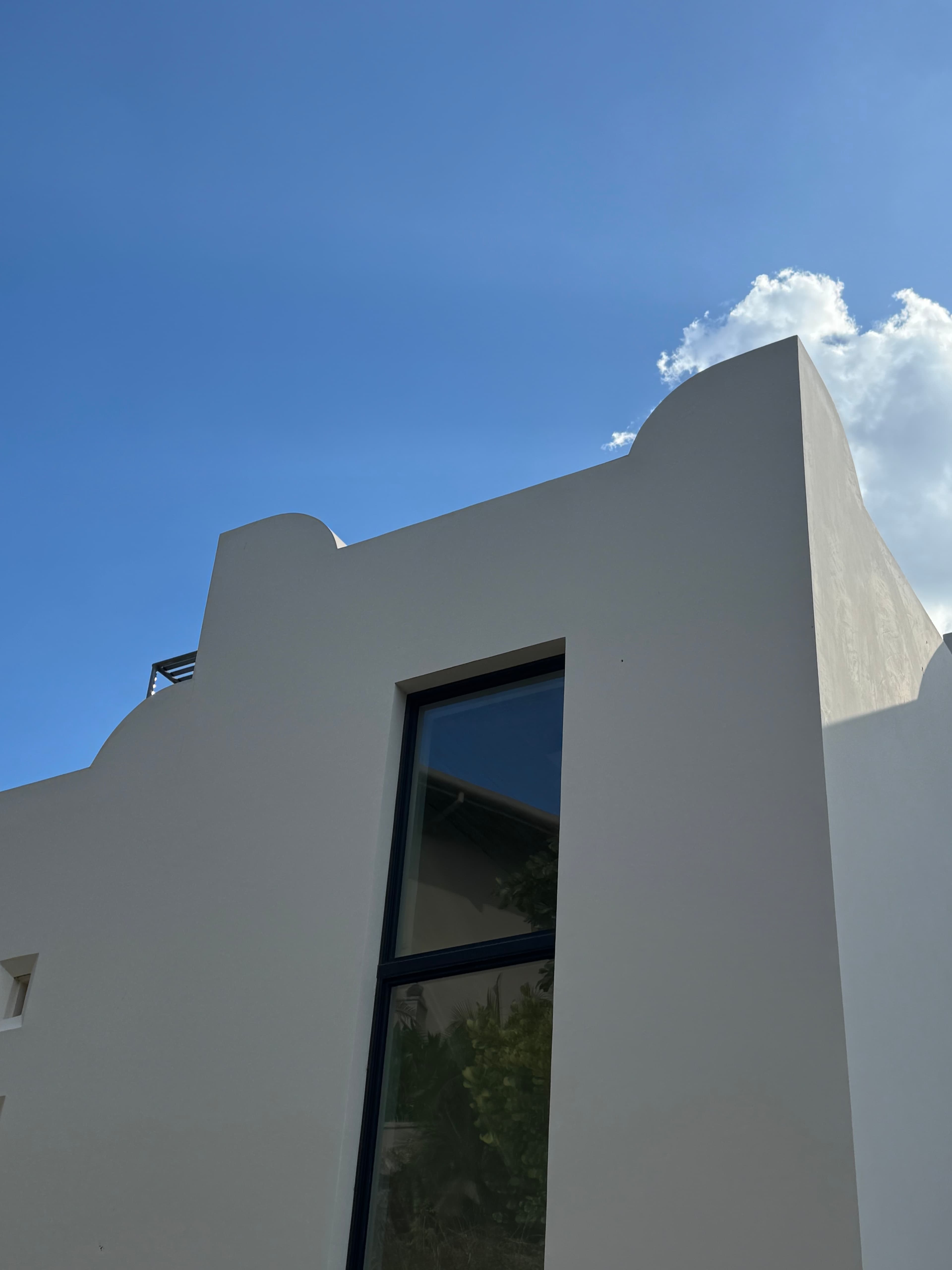 Upper exterior of Villa Luciérnaga against a blue Costa Rican sky -- the scalloped white parapet whose silhouette is echoed in the corridor sconces below